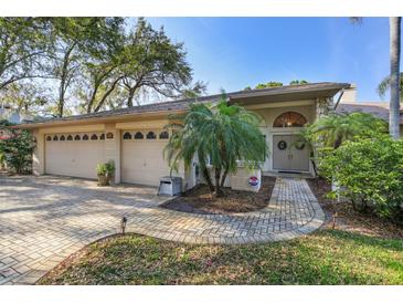 Charming home featuring a brick walkway, a three-car garage, and beautiful landscaping with mature trees at 8823 Crescent Forest Blvd, New Port Richey, FL 34654