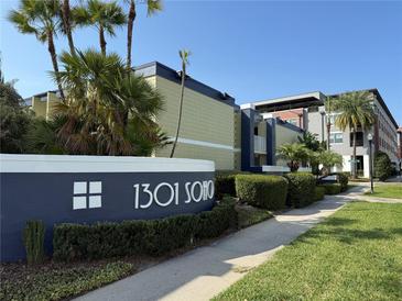 The condo is a multi-story property with a well-kept lawn, mature trees, and a sign that says 