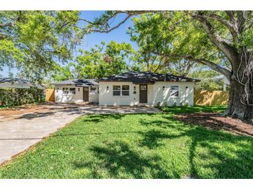 Charming single-story home with white exterior, dark roof, and mature trees at 1104 S Lois Ave, Tampa, FL 33629