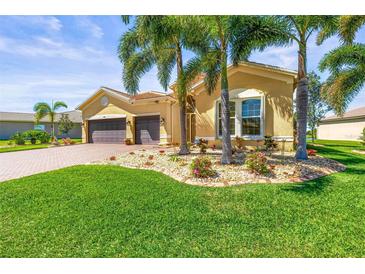 Inviting single-story home featuring a two-car garage, lush landscaping, and mature palm trees at 5073 Stone Harbor Cir, Wimauma, FL 33598