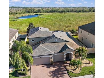 Stunning aerial view of a home with lush landscaping, a brick driveway, and a serene pond in the background at 13325 Sunset Shore Cir, Riverview, FL 33579