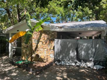 Exterior of house featuring a stone facade, banana tree, covered entrance, and tarped car port at 2610 E 26Th Ave, Tampa, FL 33605