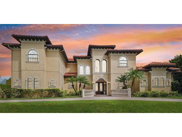 Stunning Mediterranean-style home featuring a tile roof, arched windows, and lush landscaping against a colorful sunset sky at 17005 Madres De Avila, Tampa, FL 33613