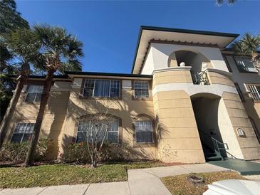 Low angle shot of a tan condo with tropical landscaping, green stairs and a light-colored balcony against a clear blue sky at 17114 Carrington Park Dr # 207, Tampa, FL 33647