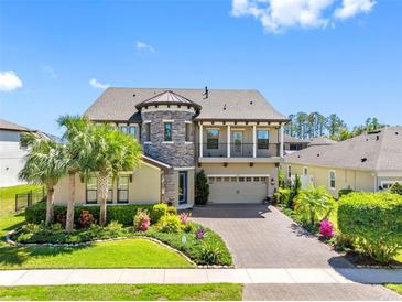 Two-story home featuring a brick driveway, manicured lawn, mature palm trees, and stone accents on the facade at 19412 Lonesome Pine Dr, Land O Lakes, FL 34638