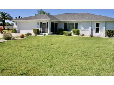 Well-maintained single-story home featuring lush lawn, neutral paint, tidy landscaping, attached garage, and a barrel tile roof at 22322 Tennyson Ave, Port Charlotte, FL 33954