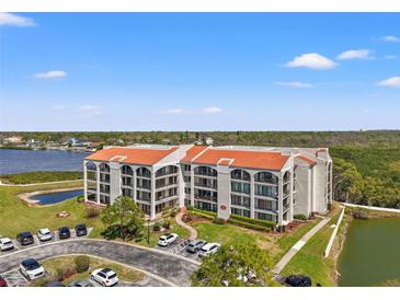 Beautiful condo building with a red tile roof and lovely landscaping, near a pond and parking area at 234 Mariner Dr # 234, Tarpon Springs, FL 34689
