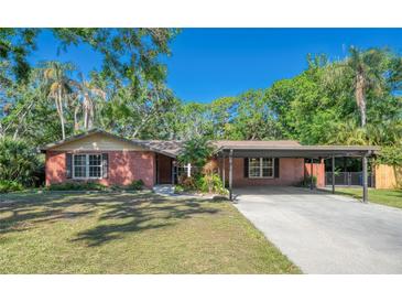Charming brick home with a carport and a well-manicured lawn, surrounded by lush greenery and mature trees at 8136 Honeybee Ln, Tampa, FL 33635