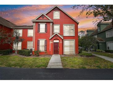 Charming red two-story townhome with manicured lawn and beautiful sunset, creating a warm and inviting ambiance at 9118 Lake Chase Island Way # 9118, Tampa, FL 33626