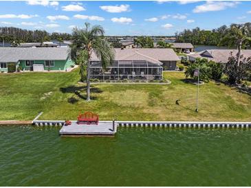 Waterfront backyard features a fishing dock with bench, large, screened lanai, and lush green lawn at 1804 Bunker Hill Dr, Sun City Center, FL 33573