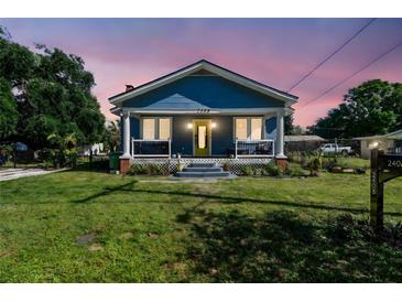 Charming blue home at dusk featuring a welcoming front porch, manicured lawn, and vibrant yellow door at 2408 Linsey St, Tampa, FL 33605