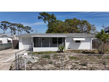 Charming white one-story home featuring a screened-in porch, attached garage, and a partially fenced yard at 2122 Holiday Dr, Holiday, FL 34691