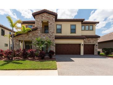 Beautiful two-story home featuring stone accents, a three-car garage, and a well-manicured lawn with palm trees at 11966 Climbing Fern Ave, Riverview, FL 33579