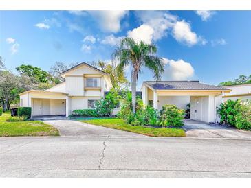 Inviting two-story home featuring a well-manicured lawn, lush landscaping, and dual carports for ample parking at 2581 Forest Run Ct, Clearwater, FL 33761