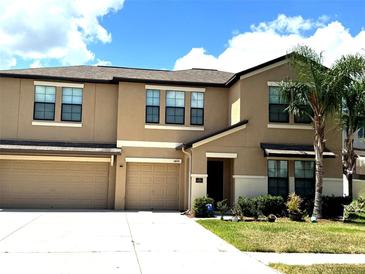 Two-story townhome with a beige exterior, well-maintained landscaping, and an attached two-car garage at 14050 Arbor Pines Dr, Riverview, FL 33579