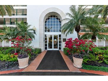 Elegant building entrance featuring a grand archway, manicured landscaping, and vibrant red flower bushes at 4750 Dolphin Cay S Ln # 209, St Petersburg, FL 33711