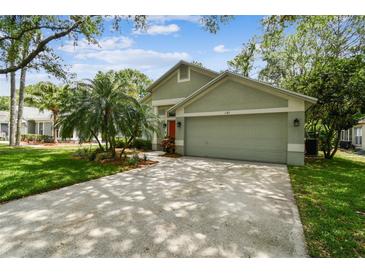 Charming home showcasing an attached garage, well-kept lawn, and a vibrant orange front door at 1187 Mistwood Dr, Tarpon Springs, FL 34688