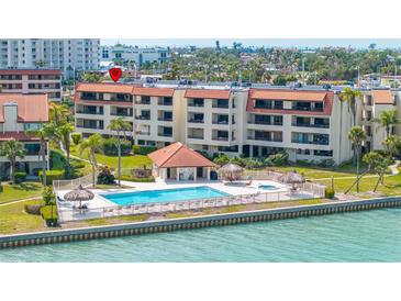 Aerial view of the condo building showcasing a luxurious swimming pool, tiki hut, and scenic waterfront at 103 1St E St # 115, Tierra Verde, FL 33715