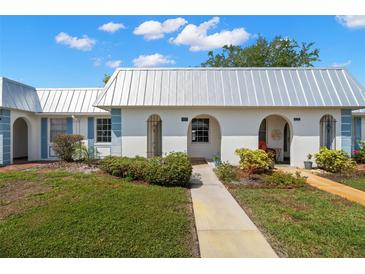 Charming villa featuring a pristine white exterior, a metal roof, and delightful landscaping under a beautiful blue sky at 4227 Glissade Dr, New Port Richey, FL 34652