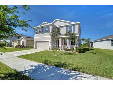 Charming two-story home with a well-manicured lawn, gray facade, and a two-car garage under a clear blue sky at 5325 Thistle Field Ct, Wesley Chapel, FL 33545