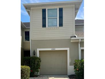 Beige two-story townhome featuring a one-car garage, blue shutters, and landscaped greenery at 10943 Verawood Dr, Riverview, FL 33579