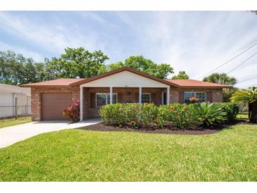 Charming brick home featuring a well-manicured lawn, flowering bushes and an attached one-car garage at 4812 Wynwood Dr, Tampa, FL 33615
