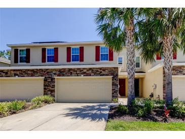 Inviting townhome with tan exterior, stone accents, two-car garage, and beautiful landscaping with palm trees at 13217 Canopy Creek Dr, Tampa, FL 33625