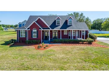 Charming red two-story home with a covered porch and beautifully landscaped front yard at 14807 Capps Estates Ln, Wimauma, FL 33598