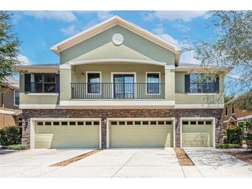 Two story home featuring a balcony, light green stucco, stone accents, and a three car garage at 5714 Kingletsound Pl, Lithia, FL 33547