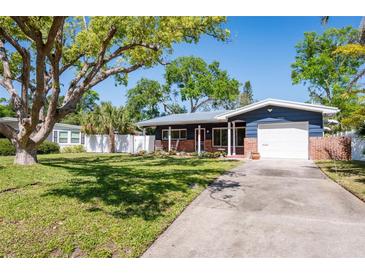 Charming home featuring a lush green lawn, mature shade trees, and a quaint front porch with a rocking chair at 2019 Inner S Cir, St Petersburg, FL 33712