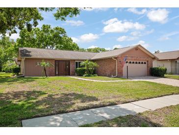 Charming single-story home featuring a brick facade, manicured lawn, and mature trees under a blue sky at 2859 Thistle N Ct, Palm Harbor, FL 34684