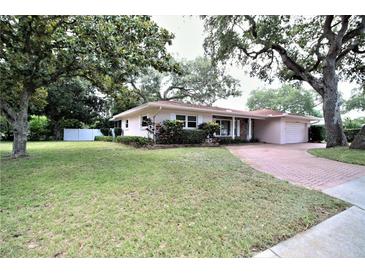 Charming single-story home with a well-manicured lawn, brick driveway, and mature trees at 1001 Brookside Dr, Clearwater, FL 33764