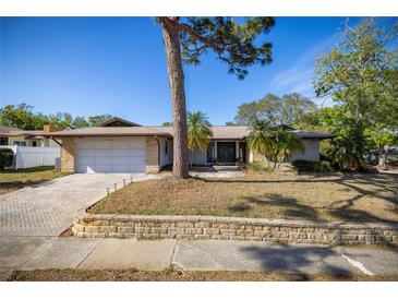 Charming single-story home with a well-manicured lawn, mature trees, brick driveway, and a two-car garage at 2932 Sweetgum S Way, Clearwater, FL 33761