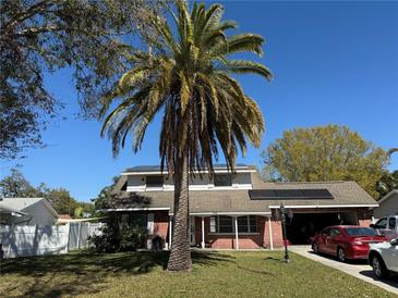 Charming two-story home with a lush green lawn, palm tree, and solar panels on the roof at 12431 Monarch Cir, Seminole, FL 33772