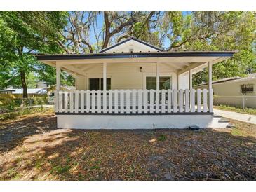 Charming home featuring a welcoming covered front porch with white picket fence and lush trees overhead at 8215 N 12Th St, Tampa, FL 33604