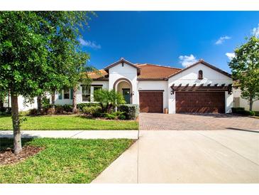 Charming single-story home with a well-manicured lawn, lush landscaping, and a brick-paved driveway at 16913 Clear Cork Dr, Wimauma, FL 33598
