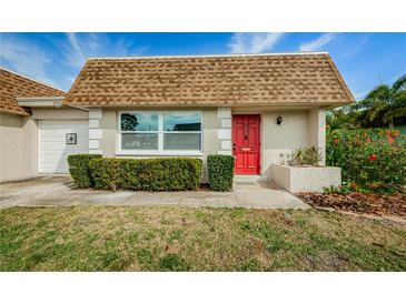 Charming single-story home featuring a red front door, manicured landscaping, and a well-maintained lawn at 6935 Monte Carlo N, Pinellas Park, FL 33781