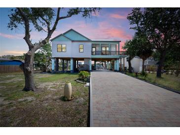 Beautifully elevated coastal home featuring a brick paved driveway, multiple balconies, and professionally landscaped yard at 1827 Venetian Point Dr, Clearwater, FL 33755