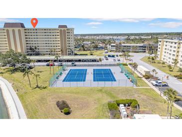Aerial view of blue tennis courts and the building with parking spots near the grassy area under a sunny, partly cloudy sky at 4725 Cove Cir # 302, St Petersburg, FL 33708