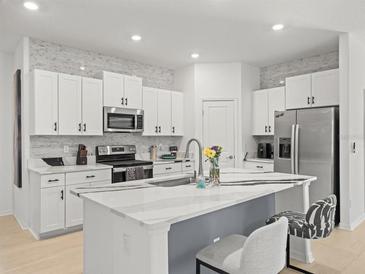 Modern kitchen features white cabinets, stainless appliances, and a large center island with stone countertops at 9617 Branching Ship Trce, Wesley Chapel, FL 33545