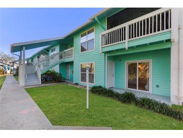 Charming two-story condo building with light-blue siding, green lawn, and a cozy outdoor porch with sliding glass door at 455 Alt 19 # 111, Palm Harbor, FL 34683
