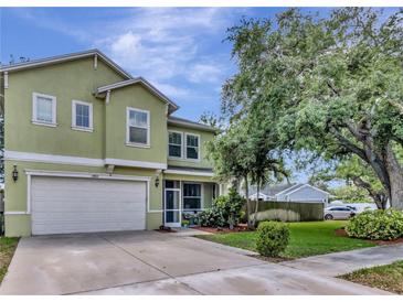 Two story home featuring an attached garage, well manicured lawn, and beautiful tree in the front yard at 3408 W Bay Ave, Tampa, FL 33611