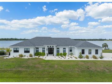 Stunning lakefront home with lush green lawn, elegant landscaping, and a classic white facade under a sunny sky at 3409 Gulf City Rd, Ruskin, FL 33570