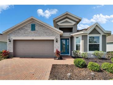 Charming home with a brick walkway, gray stone accents, teal door, well-maintained landscaping, and a two-car garage at 11773 Little River Way, Parrish, FL 34219