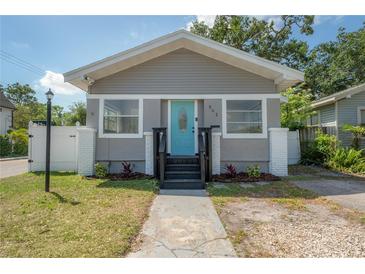 Charming bungalow featuring a bright blue front door, fresh landscaping, and updated siding at 302 W Hilda St, Tampa, FL 33603