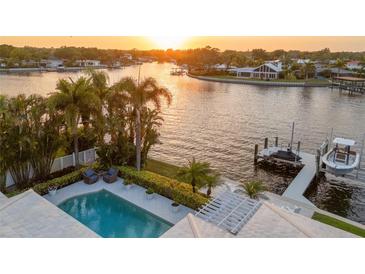 Aerial view of waterfront property featuring a pool, dock, and lush landscaping at sunset at 935 Eden Isle Ne Dr, St Petersburg, FL 33704