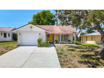 Charming single-story home features a cheerful yellow door, attached garage, and well-maintained lawn at 10819 Los Santos Dr, Port Richey, FL 34668