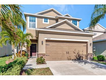 Two-story home featuring a two-car garage, stone accents and tropical landscaping at 16717 Myrtle Sand Dr, Wimauma, FL 33598