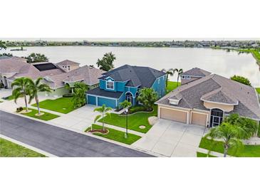 Aerial view showcases a beautiful blue home next to a lake and well-maintained landscaping at 1806 Mira Lago Cir, Ruskin, FL 33570