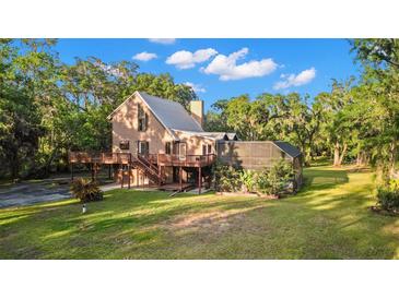 Stunning exterior view of a tan home featuring a metal roof, large deck, and screen enclosed outdoor space surrounded by lush greenery at 9298 Carr Rd, Riverview, FL 33569